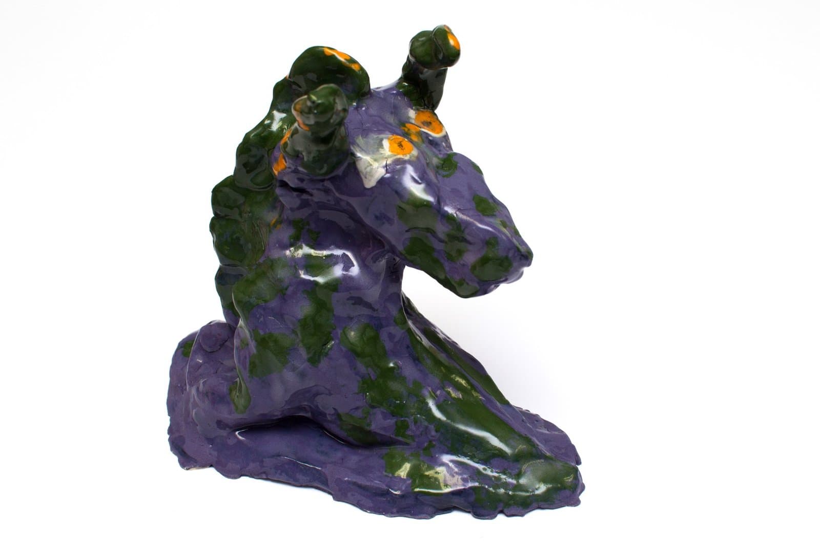 Ceramic sculpture of seated figure with horned head in purple and green glazes