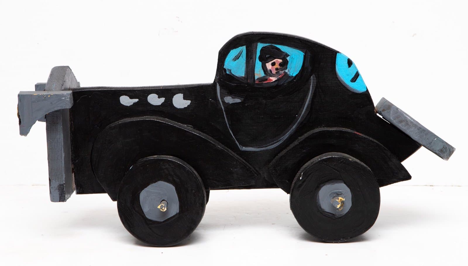 Wooden toy car sculpture painted black with blue accents, featuring a small portrait in the windshield