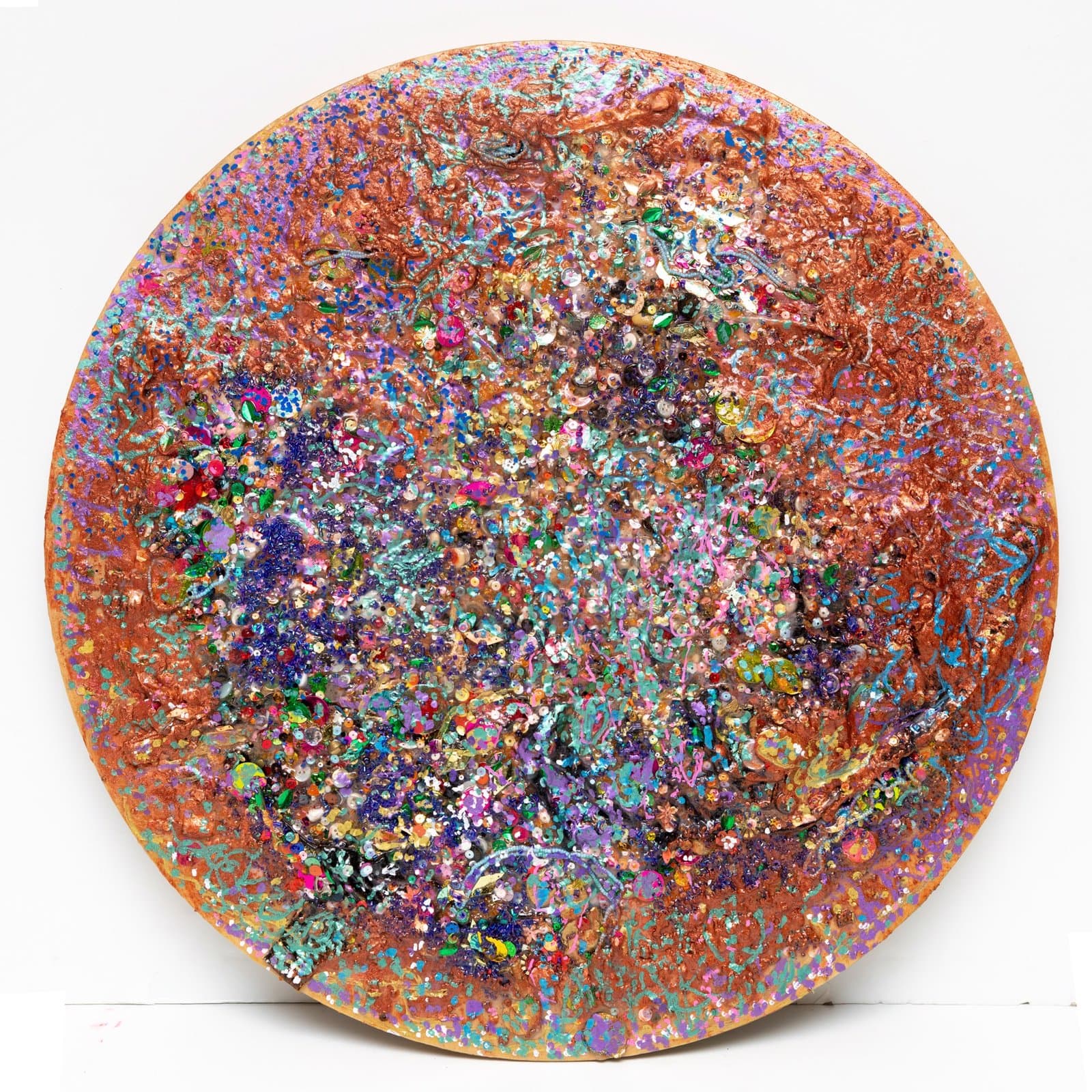 Circular mixed media artwork with dense layers of multicolored glitter, paint, and collage materials on wood panel.