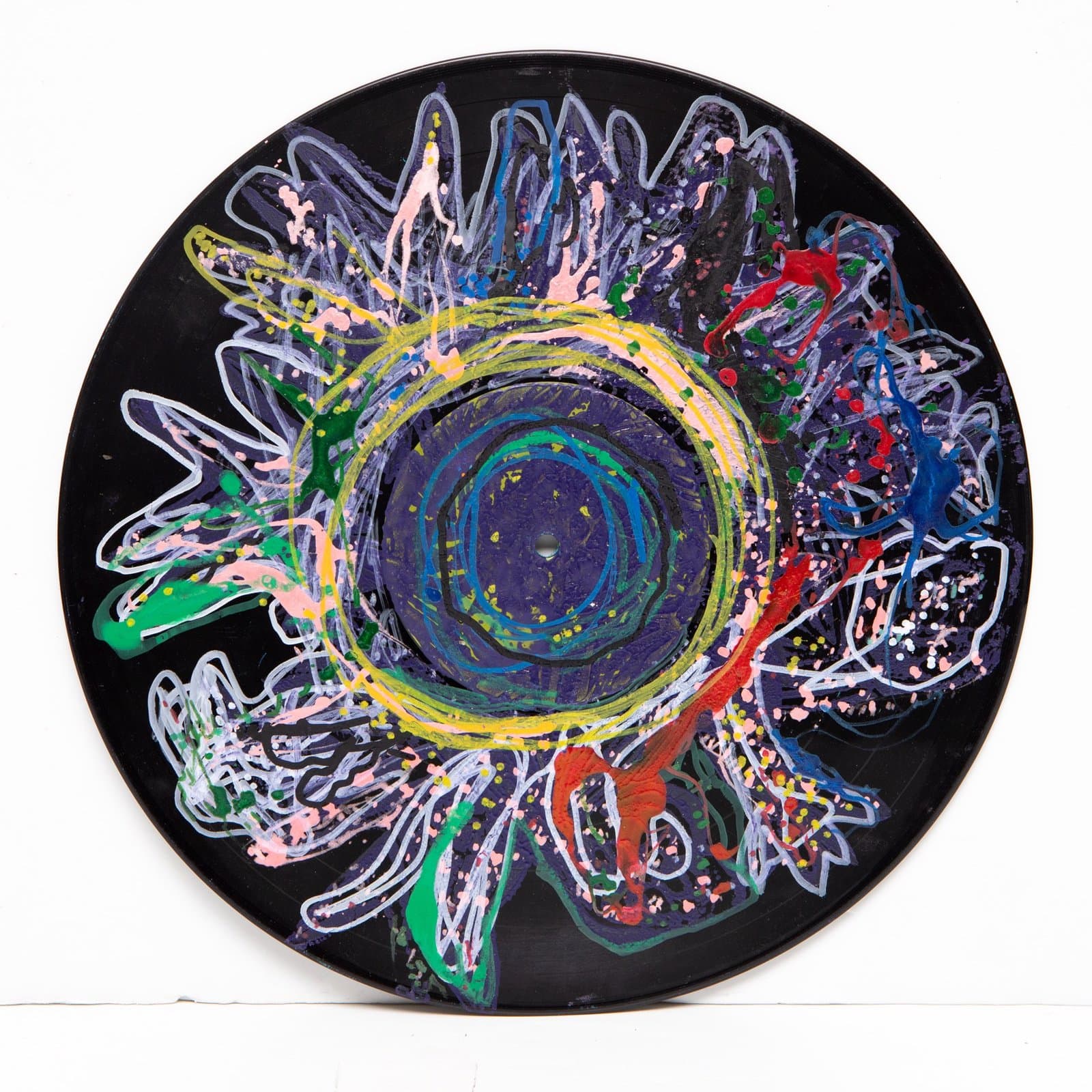 Circular painting on vinyl record with radiating floral or sun-like pattern in multicolored paint on black background.